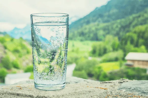 glass of water outside on table with green valley in the background